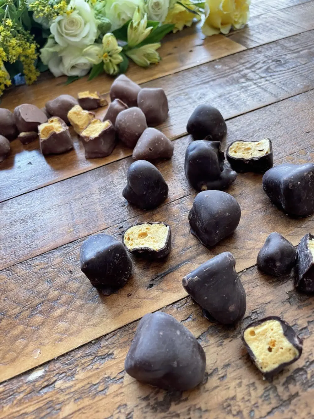 Yummycomb Nuggets of Premium Belgian chocolate covered honeycomb in bite size pieces. On a rustic wooden country able there is a range of 70% Dark chocolate orange and milk Belgian chocolate.
