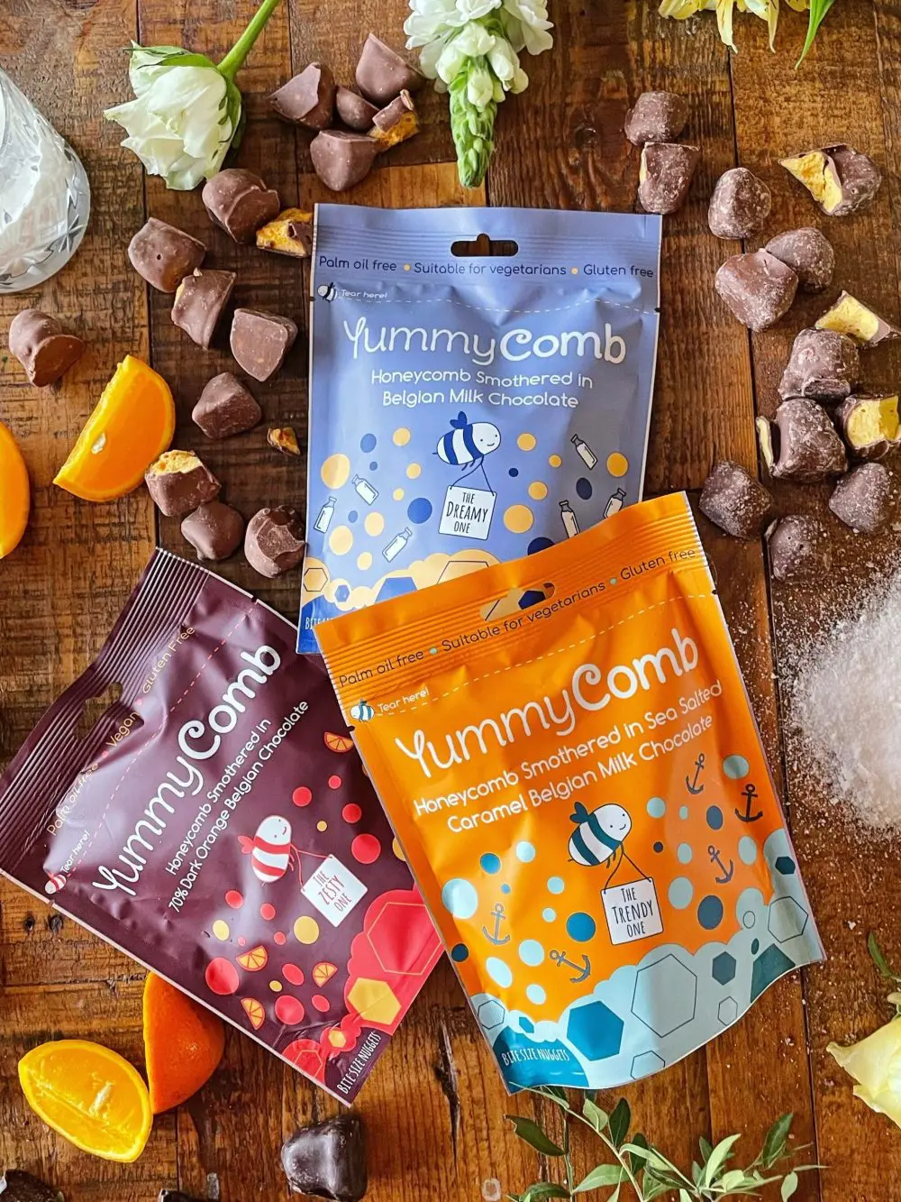 Yummycomb pouch bag range. Premium Belgian chocolate coated honeycomb. Sea Salted Caramel, Milk and 70% Dark Orange scattered on a country vintage table.